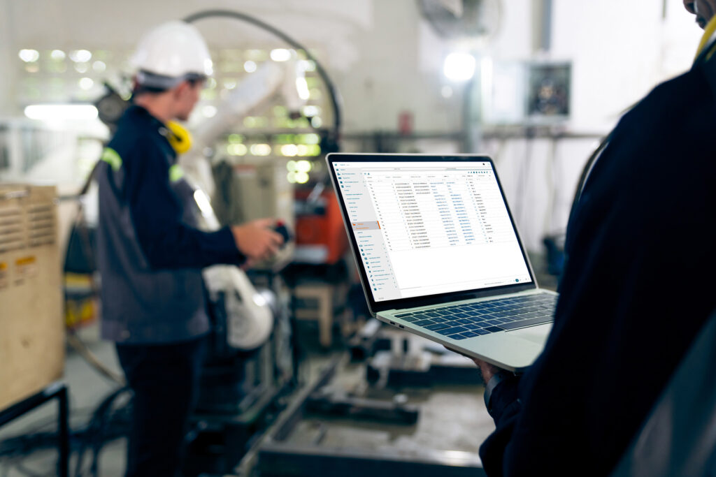Laptop z systemem Digital Twin Digitio Factory trzymany przez pracownika – w tle hala produkcyjna