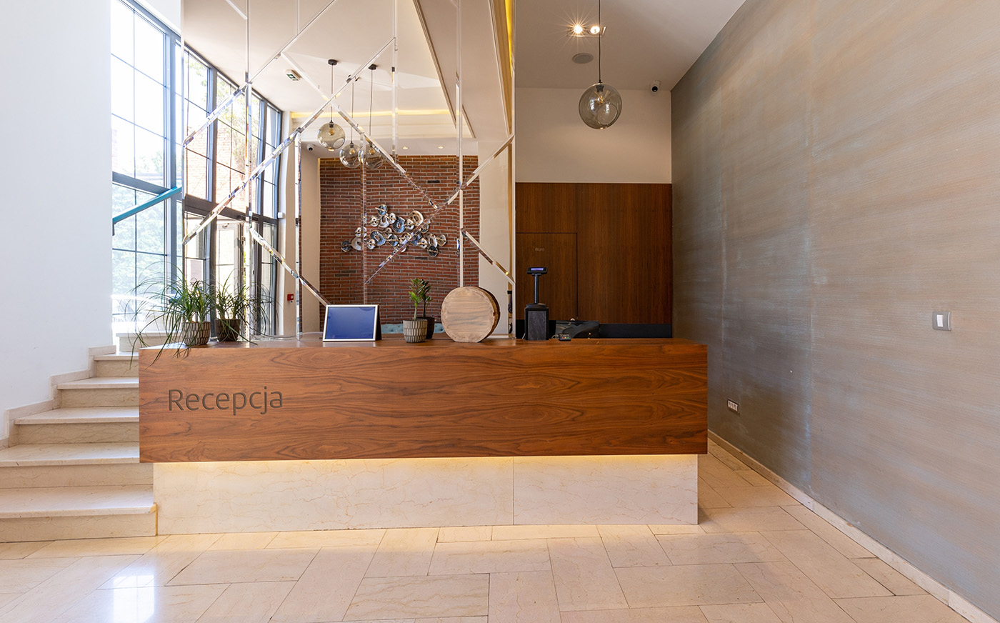 Recepcja hotelowa, biurko, kasa fiskalna, terminal, oznakowanie recepcji, schody, kwiaty