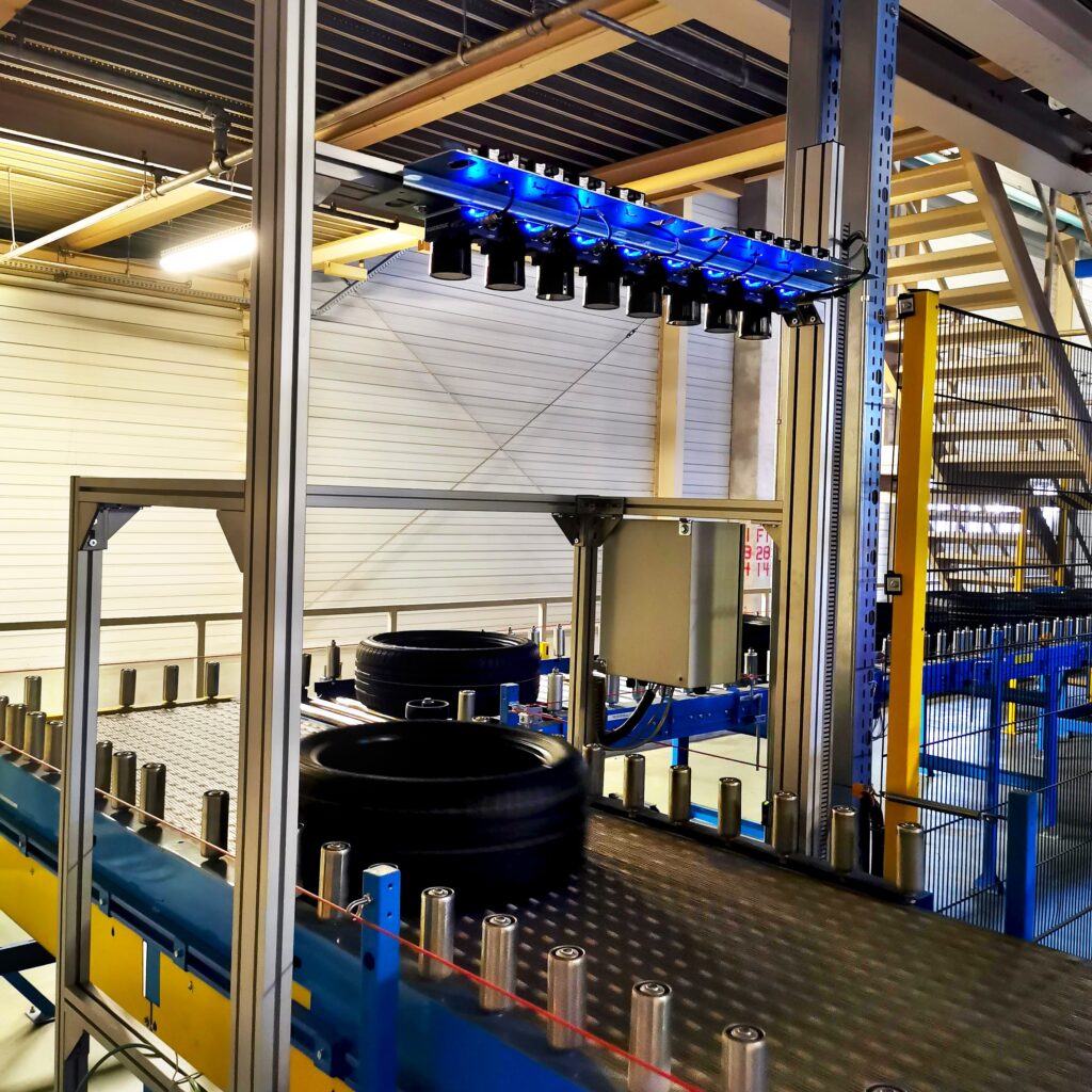 Bramka skanująca nad przenośnikiem z oponami w fabryce opon