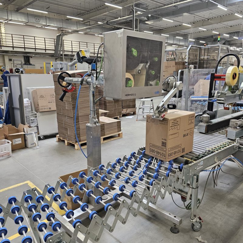 CAB Hermes Q applicator - labeling cartons on a conveyor in a warehouse
