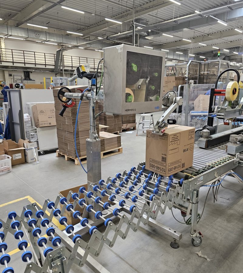 CAB Hermes Q applicator - labeling cartons on a conveyor in a warehouse