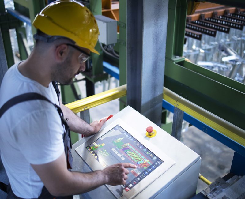 Factory worker monitoring industrial machines and production remotely in control room.