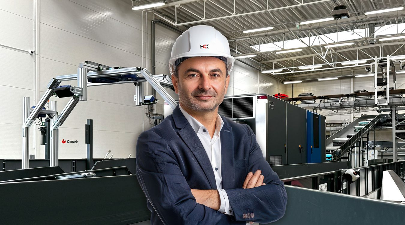 Manager centrum dystrybucji w garniturze i kasku – w tle przenośniki BHS