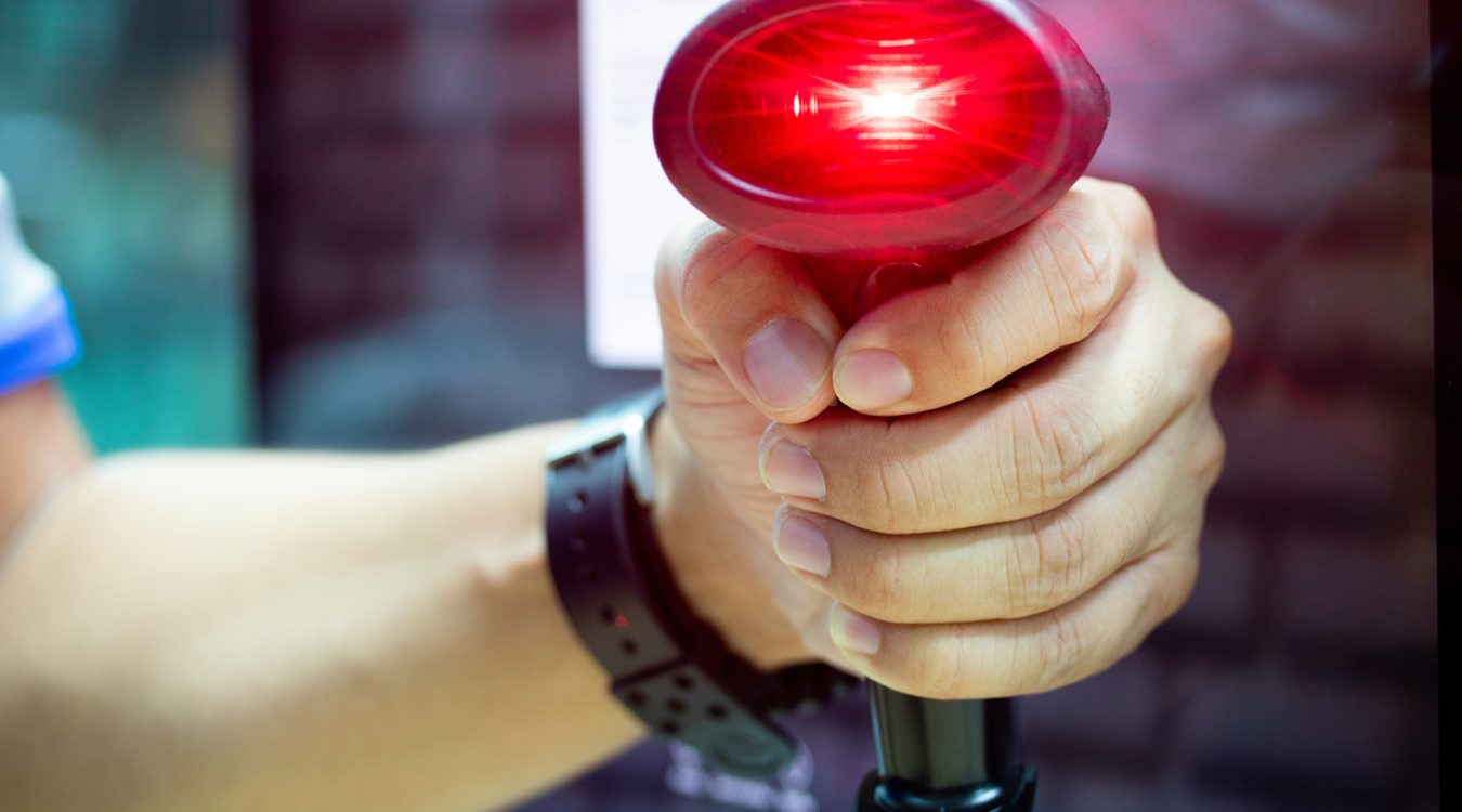 Skaner kodów kreskowych AutoID trzymany w ręku z widoczną wiązka lasera w trakcie skanowania