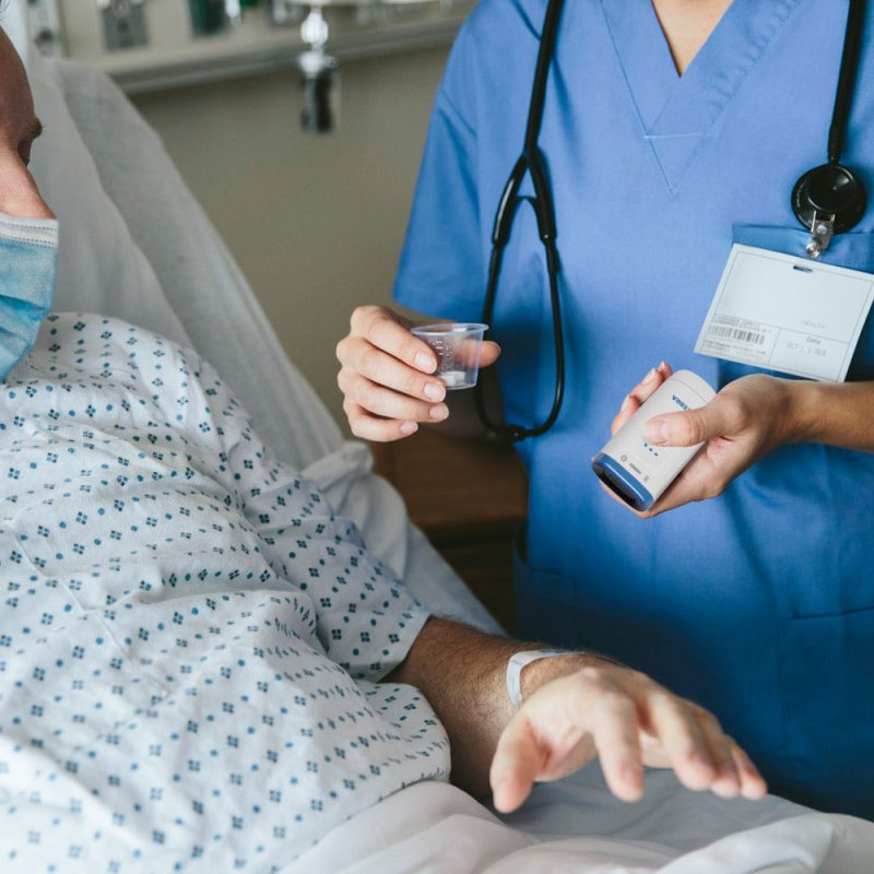 Pielęgniarka w szpitalu podaje pacjentowi lek i wykonuje skan kodu na opasce identyfikacyjnej na nadgarstku pacjenta