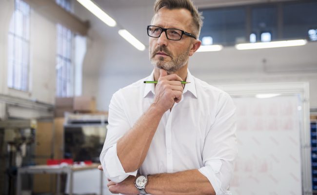 Mature businessman in factory thinking