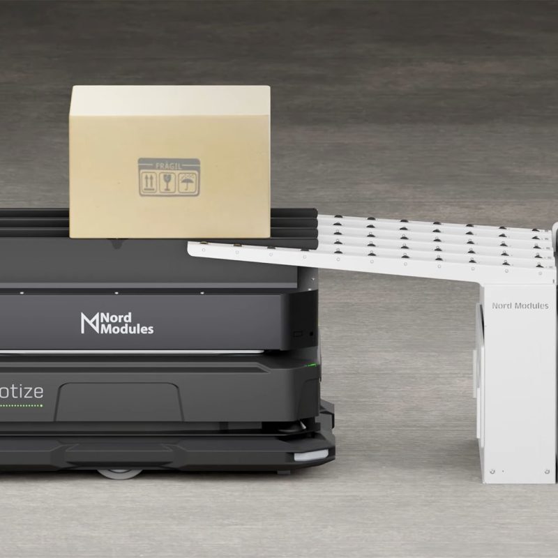 Robot AMR wyposażony w system transportowy Nord Modules odbiera karton z przenośnika rolowego